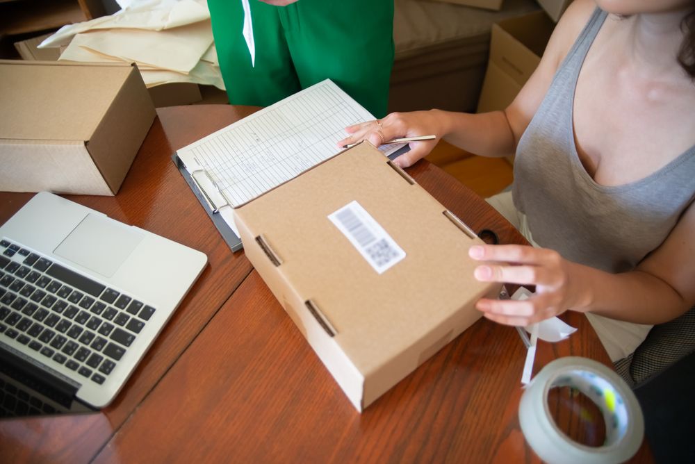 A small business owner checking an order beside a laptop and shipping boxes
